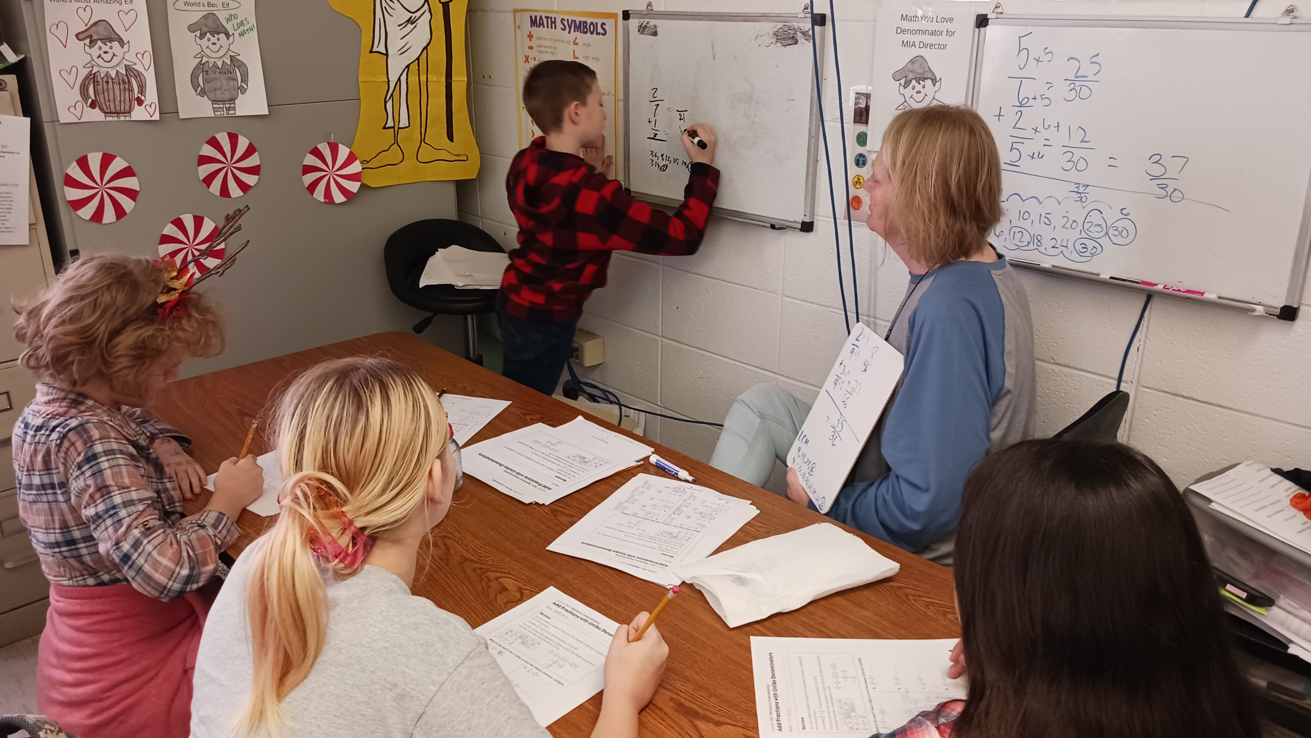 Student writing on board in front of teacher and small group