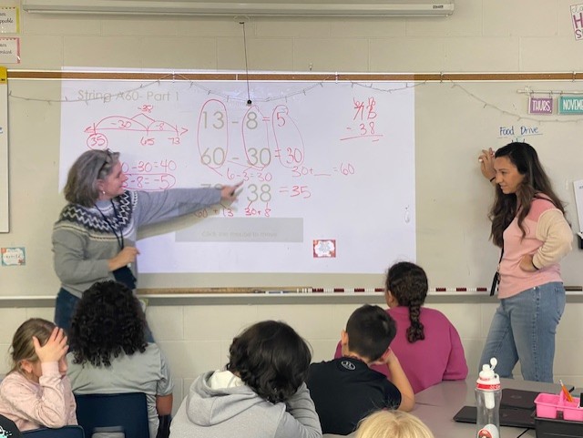 Picture of coach and teacher standing at whiteboard with math problems