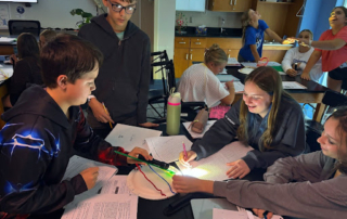 Group of middle school students work together on a light and shadow science activity using a flashlight and string on a circular model.