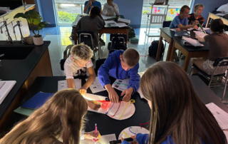 Students shine flashlights on a circular model with string lines during a classroom science activity.